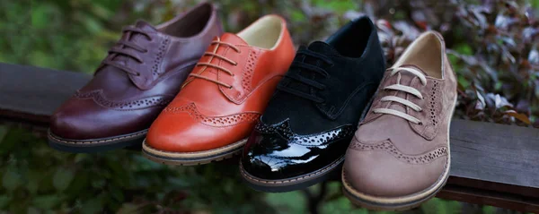 Vista da vicino di un colore un sacco di paia di scarpe, disposti su un legno, su uno sfondo del parco, copiare spazio. — Foto Stock