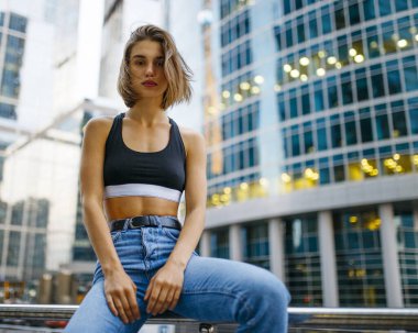 Kısa saçlı hippi bir kadın, bluz giyiyor, kot pantolon, botlar, dışarıda poz veriyor..