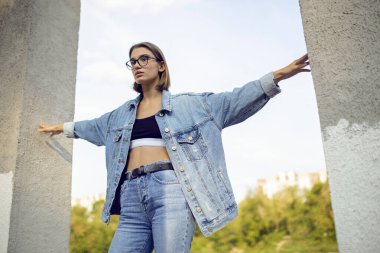 Sarışın genç bir kadının portresi, kot ve bot giymiş, dışarıda oturmuş, kollarını kaldırmış..