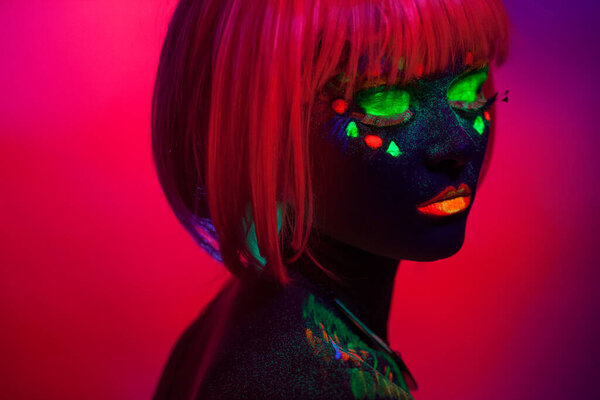 Закрыть УФ-портрет девушки с художественным цветным макияжем и оранжевым париком, изолированным оранжевым фоном.