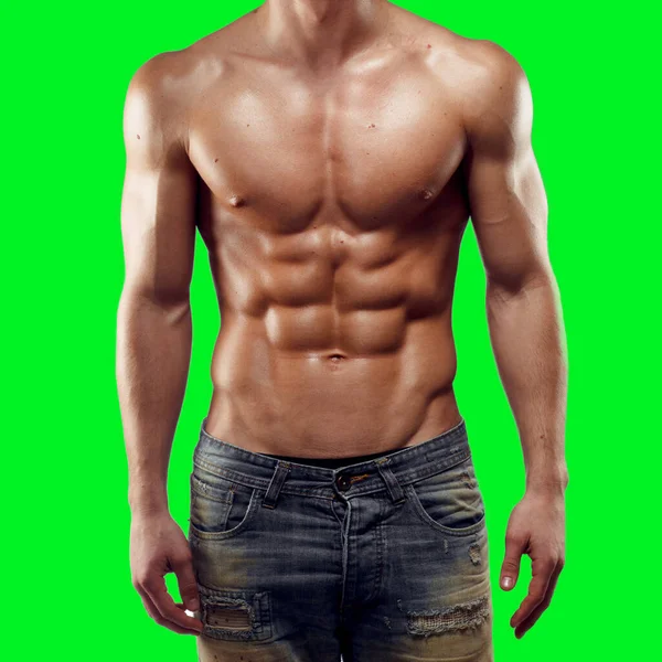 Großaufnahme eines kräftigen, athletischen, muskulösen Mannes in Jeans, der auf grünem Hintergrund steht. Zeigt Oberkörper, Sixpack-Bauch. — Stockfoto