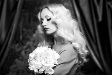 Kıvırcık saçlı, elinde çiçekle güzel bir sarışının ön portresi. Siyah beyaz arkaplan.