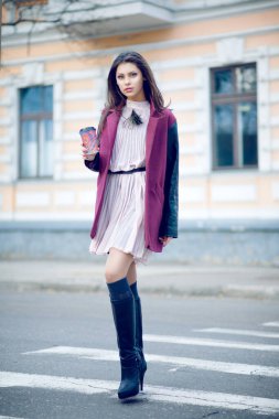 Çekici genç bir kadının bir fincan kahveyle dışarıda yürümesinin uzun bir portresi..