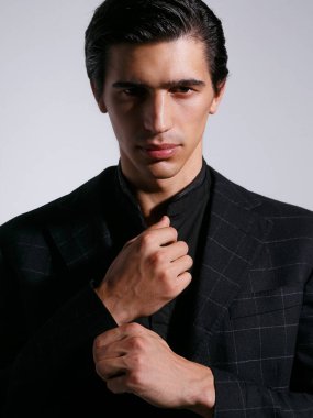 Beyaz arka planda siyah giysili, kendinden emin genç bir adam. Dikey görünüm.