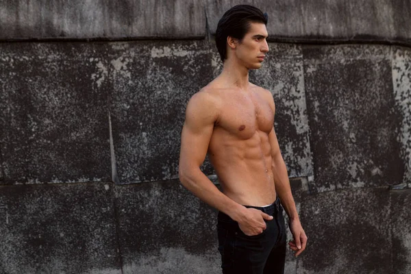 Retrato de perfil de um jovem bonito com tronco sem camisa perto da velha parede preta. Homem saudável esportivo. — Fotografia de Stock