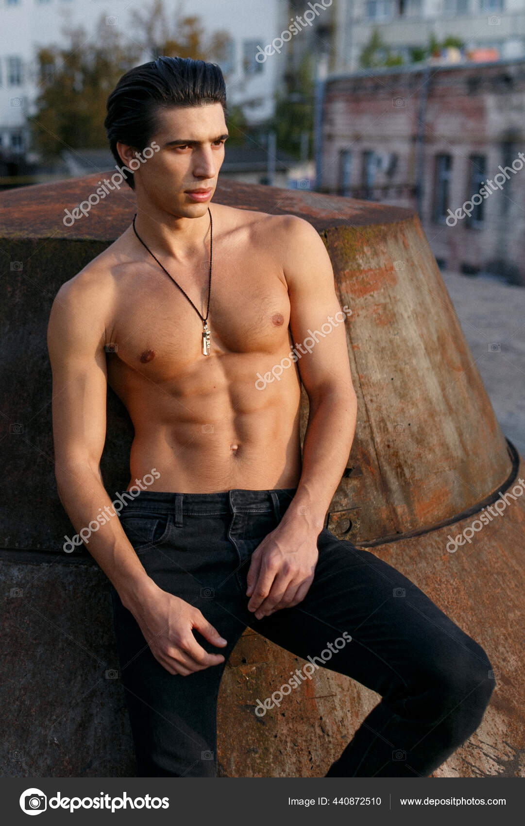Closeup of a sexy male model with tanned skin posing with naked torso outside, showing six pack