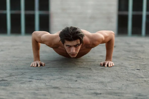 Joven músculo guapo hombre hace flexiones con desnudo torso. — Foto de Stock