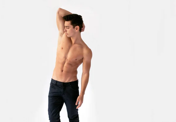 Sexy jovem com torso cortado em jeans pretos, posando em estúdio com a mão levantada, isolado em um fundo branco. — Fotografia de Stock