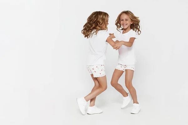 Glimlachend grappig tweelingzusjes in witte kleren dansen geïsoleerd op witte achtergrond kinderen studio portret. — Stockfoto