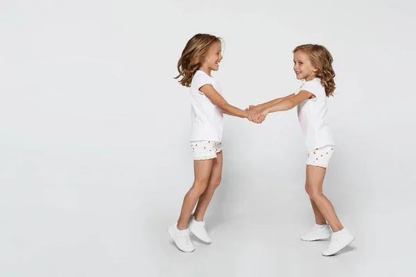 Gelukkig grappig tweelingzusjes in wit kleding dansen geïsoleerd op wit achtergrond. — Stockfoto