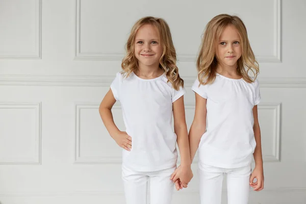 Två små barn flickor i vita kläder isolerad på vit bakgrund. Barndomskoncept. Tvillingflickorna håller varandra i handen. — Stockfoto
