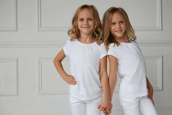 Две сестры-близнецы в белой одежде держатся за руки изолированные на белом фоне. Концепция детского образа жизни. — стоковое фото