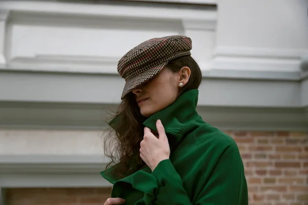 Perfil retrato de uma mulher elegante com cabelo encaracolado, vestindo casaco verde e chapéu, detém colarinho, fundo do edifício velho. — Fotografia de Stock