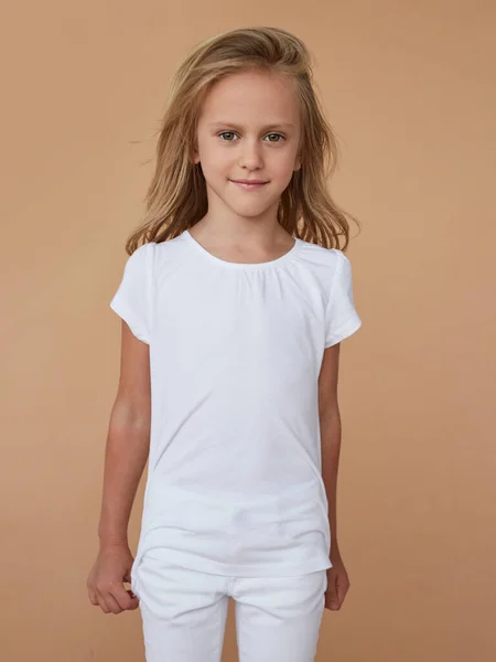 Voorportret van een mooi klein timide meisje met golvend haar, gekleed in witte kleren. Verticaal overzicht. — Stockfoto