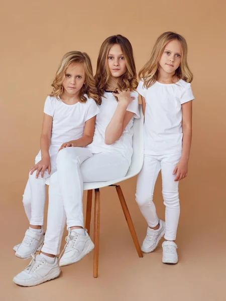 Volledige afbeelding van drie zussen met blond krullend haar gekleed in witte kleren, geïsoleerde beige achtergrond. — Stockfoto