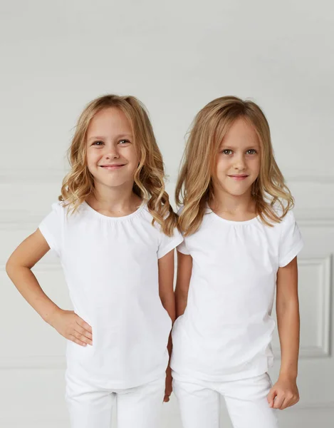 Twee kleine lachende kinderen meisjes in witte kleren geïsoleerd op witte achtergrond. Tweeling meisjes houden ze hand in hand. — Stockfoto