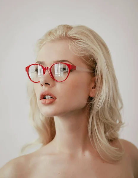 Retrato de cerca de una sensual mujer rubia con maquillaje usando anteojos rojos, mirando al costado, sobre fondo blanco. — Foto de Stock