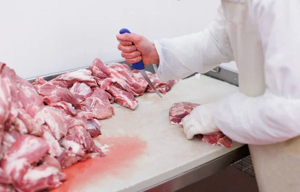 Un trabajador usa en forma blanca en la fábrica de carne, picó una carne de res en pedazos en la mesa de trabajo, la industria de procesamiento de alimentos. — Foto de Stock