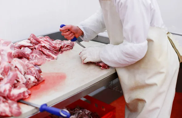 Καλλιεργημένη εικόνα ενός εργάτη σε εργοστάσιο κρέατος, τεμαχισμένο ένα φρέσκο βόειο κρέας σε κομμάτια στο τραπέζι εργασίας, βιομηχανία μεταποίησης. — Φωτογραφία Αρχείου
