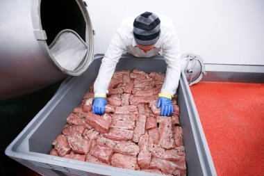 A worker in the meat factory, he arranges pieces of meat marinated in spices, a food processing and production industry. clipart