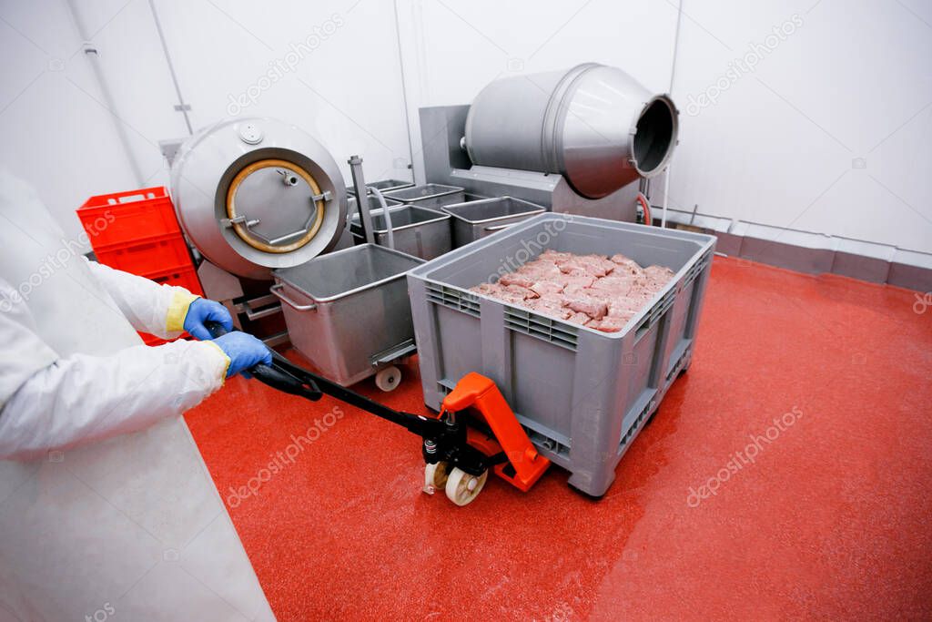 Worker at a meat factory, pulls a load on which are crates of raw spicy meat. Production of products of animal origin.