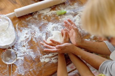 Cropped image of a female and kid hands holding dough in heart shape top view. Baking ingredients on the wooden table. clipart