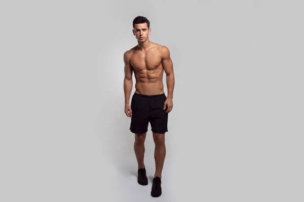 Full längd bild av en självsäker ung man skjorta utan överkropp visar sex pack abs, isolerad grå bakgrund. — Stockfoto
