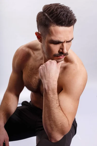 Hombre guapo con bigote, sin camisa, mostrando bíceps y tríceps, sentado en un tronco de árbol, sobre fondo blanco. — Foto de Stock