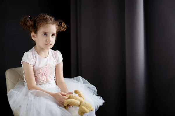 Adorable little curly girl portrait. Sad birthday, unhappy kid, seated on chair look away. Copy space.