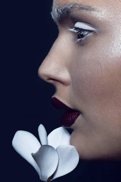 Close up profile portrait of a female model, with artistic makeup and flowers near face, isolated on a black background. Creative artistic concept.