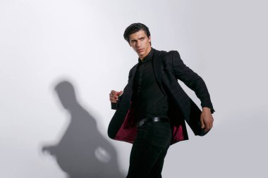 Beyaz arka planda izole edilmiş siyah takım elbiseli yakışıklı ve güçlü genç bir adamın portresi. Yatay görünüm.