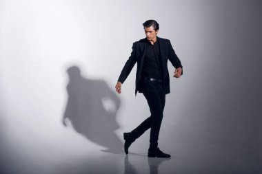 Beyaz arka planda izole edilmiş siyah takım elbiseli yakışıklı erkek modelin tam boy görüntüsü. Yatay görünüm.