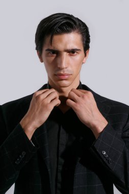 Beyaz arka planda siyah giysili, kendine güvenen yakışıklı bir gencin yakın portresi. Dikey görünüm.