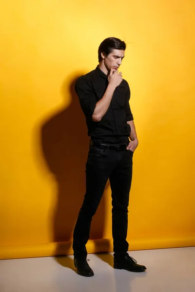 黄色の背景に黒い服を着たアスリートハンサムな強い若い男の完全な長さの肖像画 垂直表示 — ストック写真
