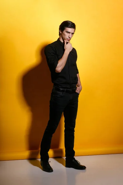 黄色の背景に黒い服を着たアスリートハンサムな強い若い男の完全な長さのイメージ 垂直表示 — ストック写真