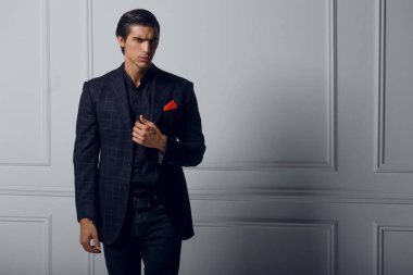 Beyaz arka planda, cebinde kırmızı ipek eşarp bulunan siyah şık takım elbiseli kendinden emin bir gencin ön portresi..