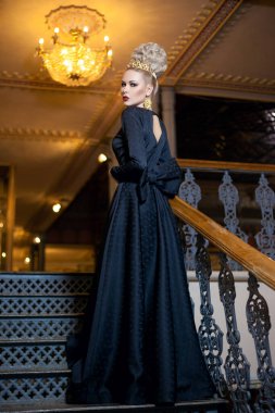 Full length image of a great young blonde woman, dressed in a long black dress, with elegant hairstyle great crown and earrings.