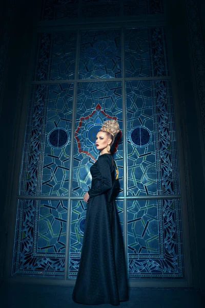 Full length view of a great young blonde female model, dressed in a long black dress, with elegant hairstyle great crown and earrings. Beauty content.