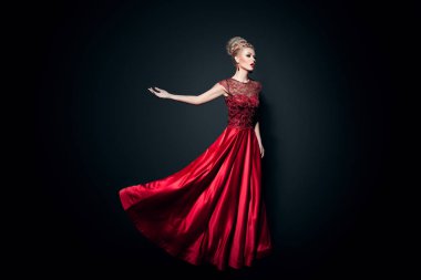 Fulll length image of a wonderful young woman dressd in a long fluing red dress with raised hands, over black background. Horizontal view.