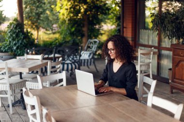 Terasta dizüstü bilgisayarda yazan masada oturan güzel genç kadının profil portresi..