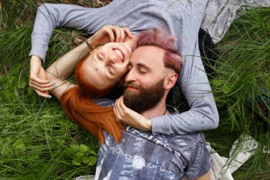 Gülümseyen bir çiftin portresi, yeşil bir çimene oturmuş, gözleri kapalı, ters dönmüş bir şekilde oturuyor..