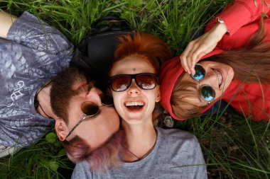 Gülümseyen, güneş gözlüklü, yeşil çimenlere uzanmış, güneş gözlüğü takan gençlerin en güzel manzarası..