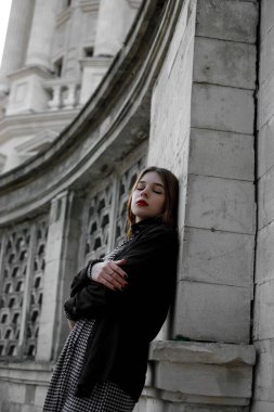 Kızıl saçlı güzel kızın portresi. Gözleri kapalı, eski binanın yanında, elleri çapraz..