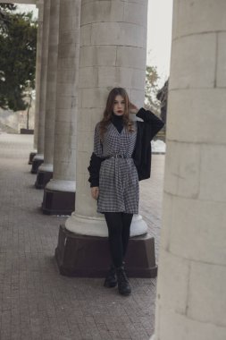 Makyajlı, kameraya bakan, sütunların yanında duran kızıl saçlı güzel kızın tam boy görüntüsü..