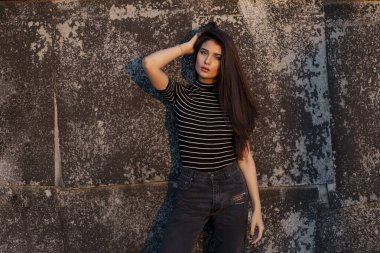 Kahverengi uzun saçlı güzel bir kadının ön görüntüsü kameraya bakıyor, eski siyah bir duvara yaslanmış..