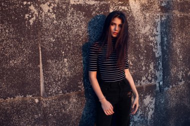 Kahverengi uzun saçlı güzel bir bayanın ön görüntüsü eski siyah bir duvara yaslanmış kameraya bakıyor. Boşluğu kopyala.