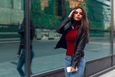 Street image. Young woman with make-up with beautiful hair in a leather jacket, girl is walking around the city.