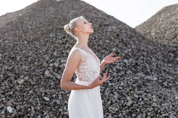 Perfil retrato de mujer con el pelo apretado en vestido de novia blanco, mantiene sus manos en el aire, sobre montones de piedras. — Foto de Stock