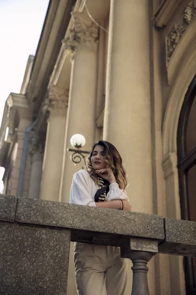 Dívka stojící na balkóně, nosit ležérní oblečení, pózovat se zavřenýma očima, izolované na starém pozadí budovy. — Stock fotografie