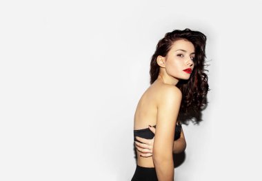 Siyah lengerie giymiş çekici esmer bir kadının arka görüntüsü gri arka plandaki kameraya bakıyor..